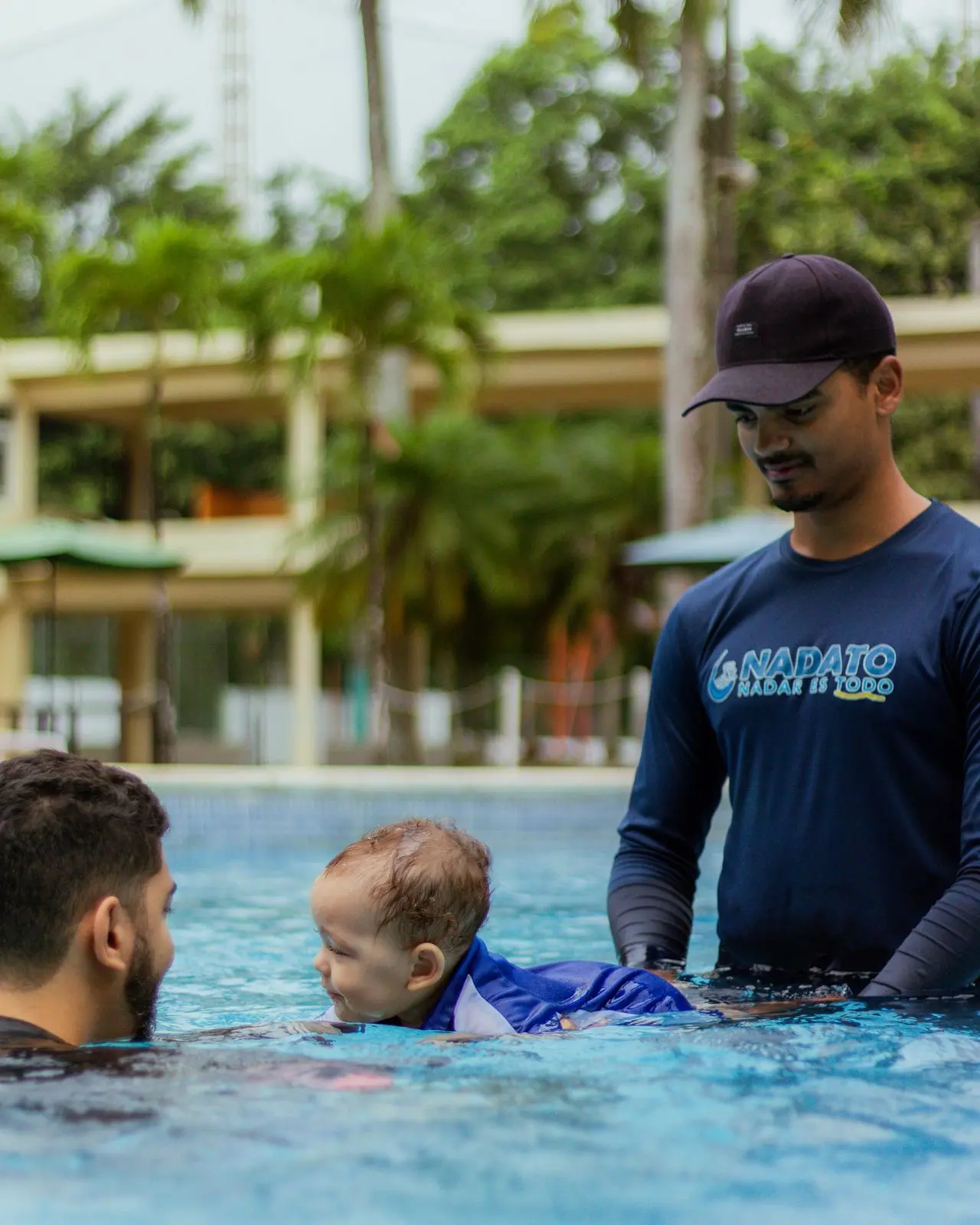 Instructor de Nadato guiando a un bebé y a su padre en la piscina